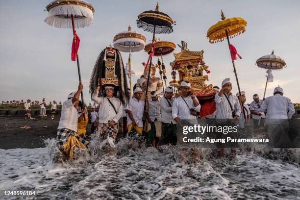 Balinese Hindus people carry sacred mask, sacred effigies and ritual paraphernalia during Melasti Ritual prior to Nyepi Day on March 19, 2023 at...