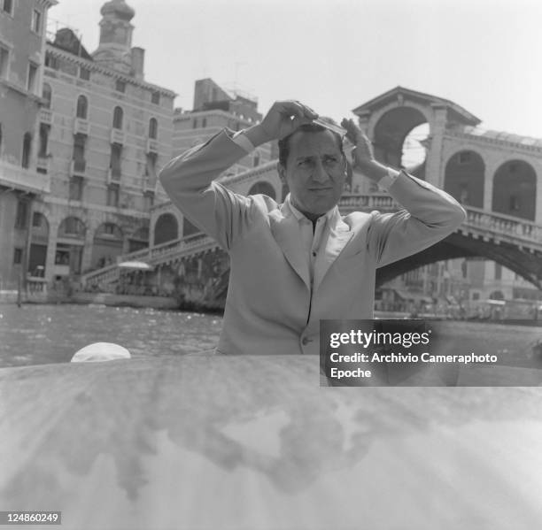 Italian actor Alberto Sordi, wearing a suit, portrayed while combing his hair on a water taxi, Rialto bridge in the background, Venice, 1959.