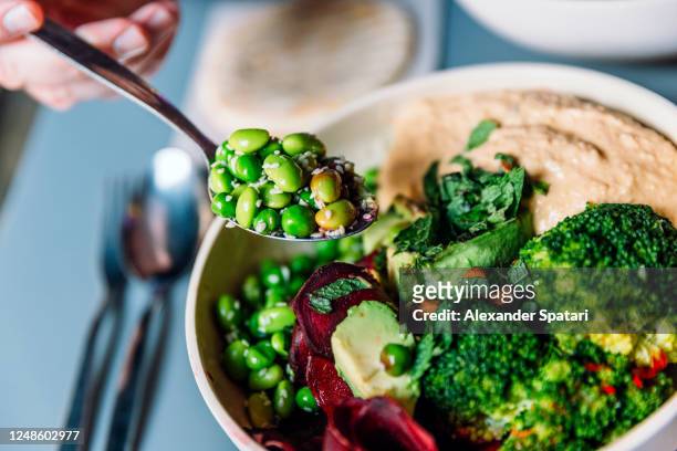 eating vegan bowl with edamame beans, broccoli, avocado, beetroot, hummus and nuts - green vegetables stock-fotos und bilder