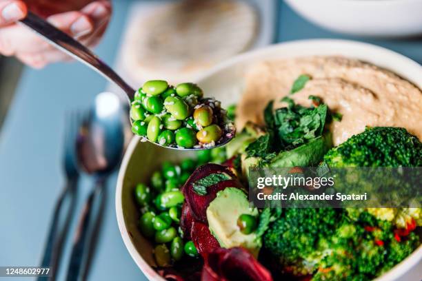 eating vegan bowl with edamame beans, broccoli, avocado, beetroot, hummus and nuts - comida vegetariana fotografías e imágenes de stock