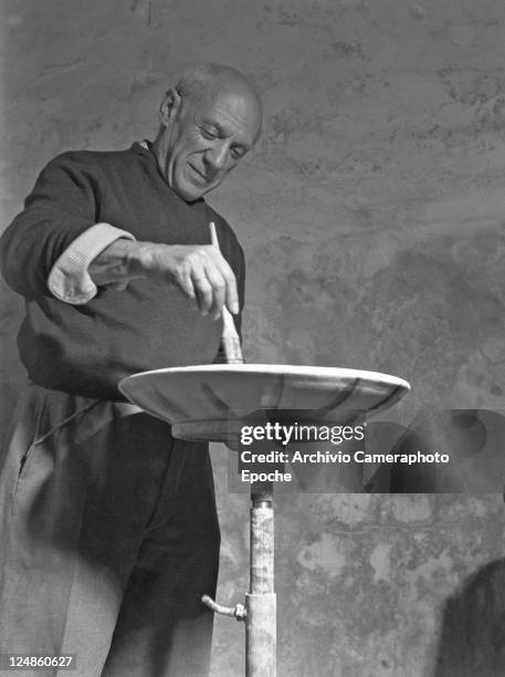 Spanish artist Pablo Picasso portrayed while decorating with paint and paintbrush one of his ceramic dishes, Paris, 1948.