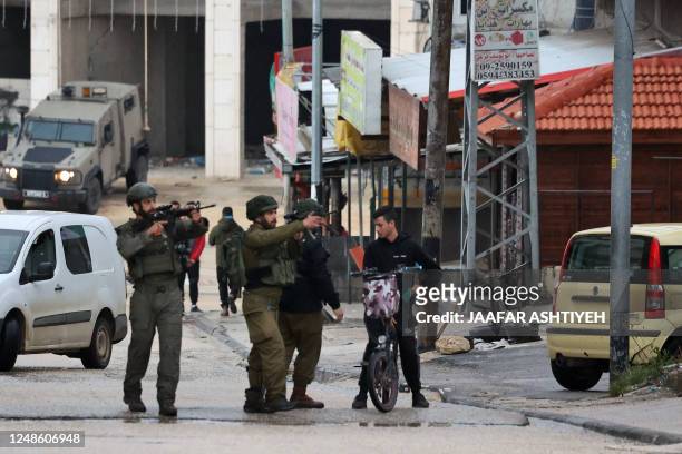 Israeli soldiers check the ID card of a Palestinian youth as they patrol the town of Huwara, in the occupied West Bank, following a reported shooting...