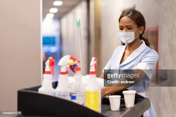 maid working at a hotel doing room service wearing a facemask and pushing a cart - hotel stock pictures, royalty-free photos & images