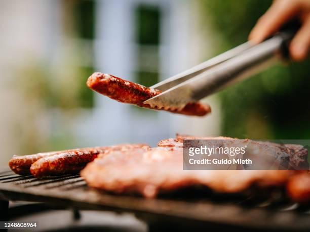 woman holding sausage on a flame grill. - sausage stock pictures, royalty-free photos & images
