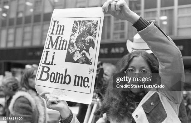 Close-up of a young woman holding up a poster with an image of a mother and child and the text "I'm Min Li, Bomb me, " during protests against the...