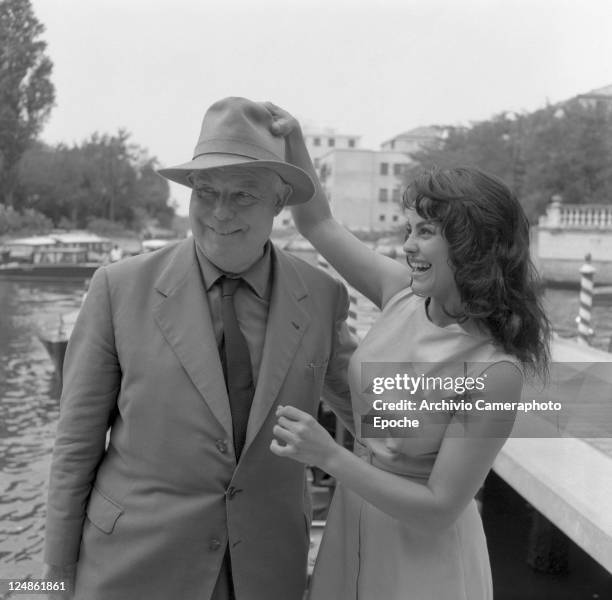 French director Jean Renoir, wearing a suit, a tie and a hat, posing fot the photographers next to the french actress Catherine Rouvel, in Lido for...