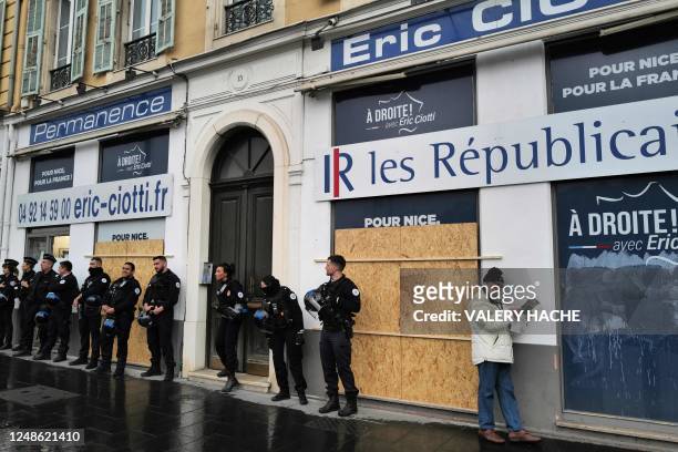 An elderly man reads a paper next to French police officers standing guard in front of the facade of the constituency office of French right-wing...