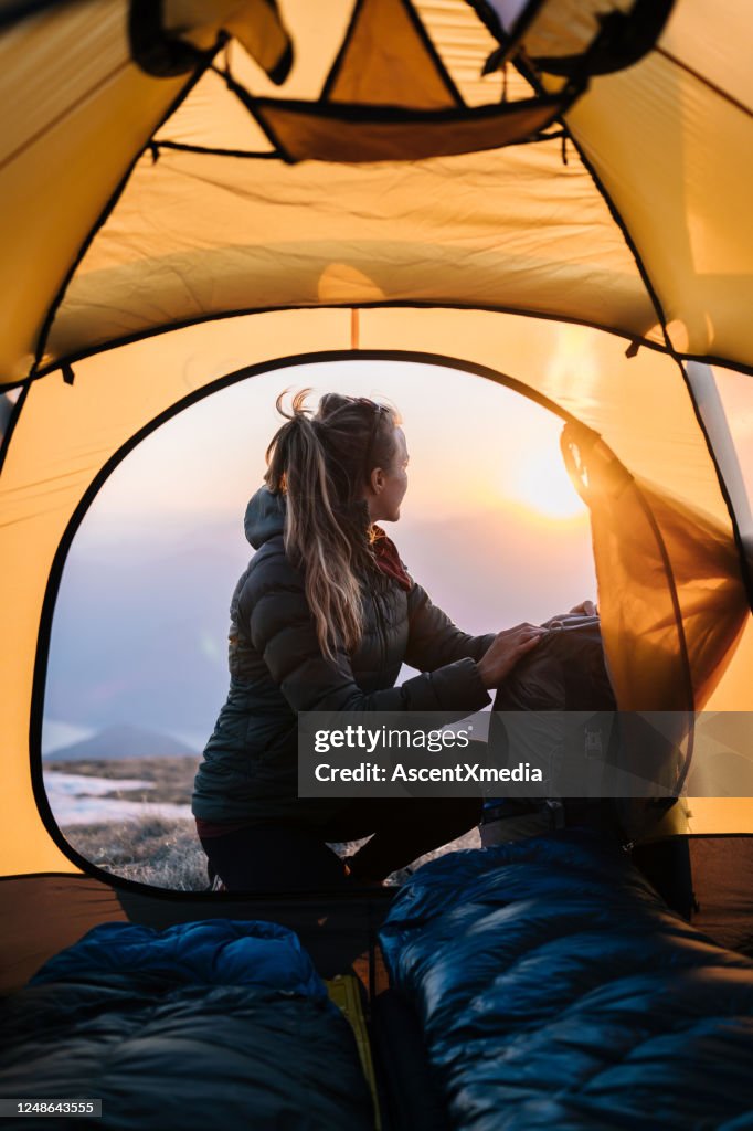 De jonge vrouw let op zonsopgang van het kamperen tent