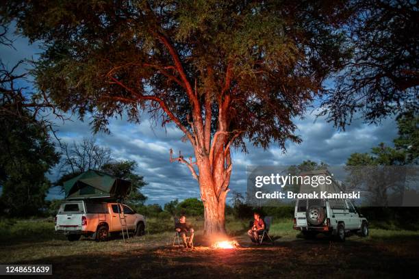 two men sit by a campfire in the african bush - camping botswana stock pictures, royalty-free photos & images