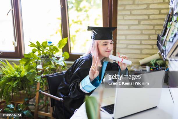 teenage girl wearing graduation gown and cap greeting her family on video call - degree stock pictures, royalty-free photos & images