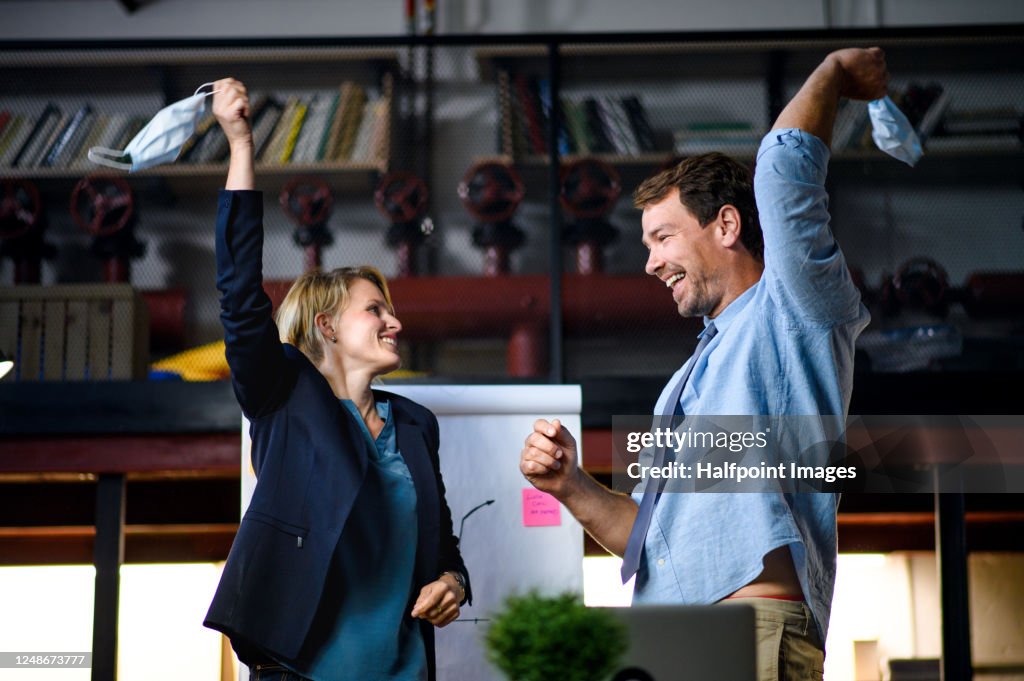 Side view of cheerful man and woman dancing indoors in office, holding face masks.