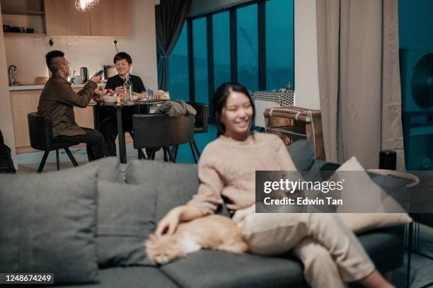 an asian chinese teenager girl watching tv at home on sofa with her pets while her mother and brother at dining room having meals at night - family tv pet stock pictures, royalty-free photos & images