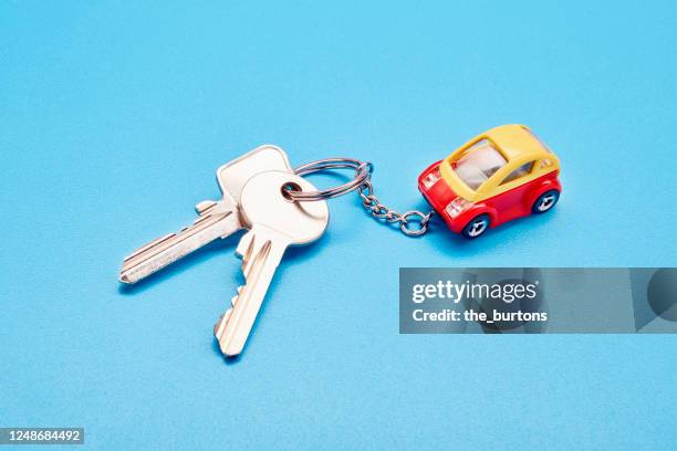 still life of a keyring with keys and a small toy car on blue background - car key stock pictures, royalty-free photos & images
