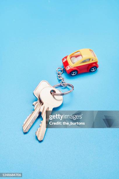 still life of a keyring with keys and a small toy car on blue background - sleutelboshanger stockfoto's en -beelden