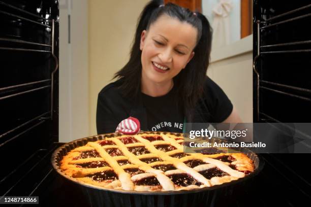 woman taking a fruit pie ( crostata ) out of the oven - crostata di frutta foto e immagini stock