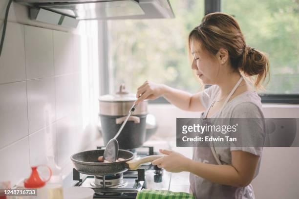 an asian chinese beautiful woman frying eggs in the kitchen getting ready for breakfast - cooking breakfast stock pictures, royalty-free photos & images