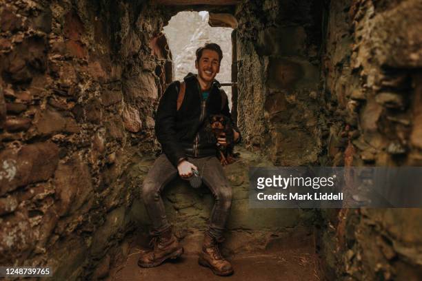 young man and his dog sitting in the ruins of dunnottar castle, scotland - dunnottar castle 個照片及圖片檔