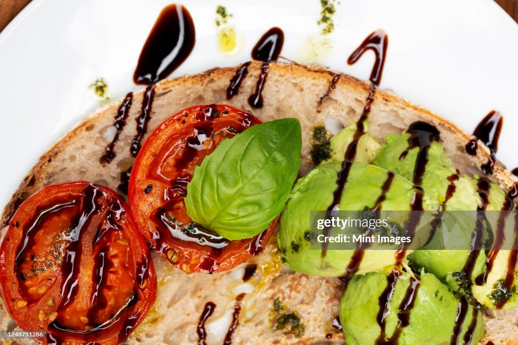 High angle close up of tomato and avocado bruschetta with balsamic vinegar reduction on a plate.