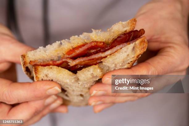 close up of person holding bacon sandwich with tomato sauce. - bacon stockfoto's en -beelden