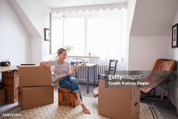 woman taking a coffee break while moving house, text messaging on mobile phone - man boxes moving home stock-fotos und bilder