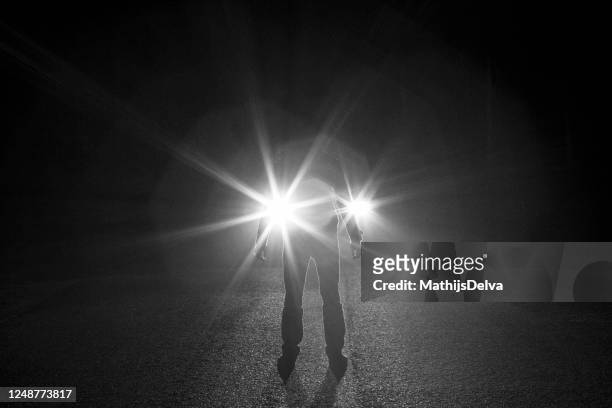 silhouette of a man standing in front of a car's headlights at night, belgium - fugitivo stock-fotos und bilder