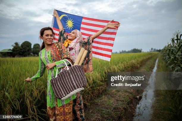 giovani donne asiatiche che sventolano la bandiera della malesia nella risaia del villaggio - malaysia independence day foto e immagini stock