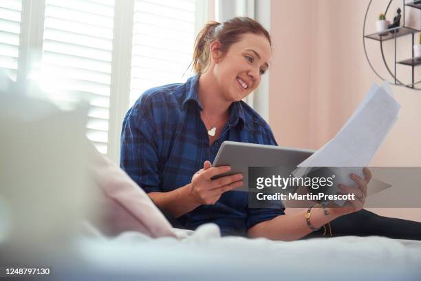 young woman sat on her bed smiling reading through paperwork - 401k statement stock pictures, royalty-free photos & images