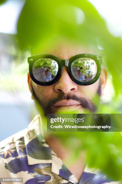 close-up of handsome standing wearing mirrored glasses surrounded by leaves - mirrored sunglasses stock pictures, royalty-free photos & images