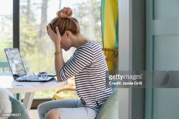 woman sitting in front of laptop with head in hands - frustration stock-fotos und bilder