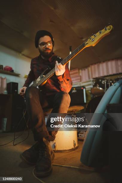young man playing bass guitar during rehearsal in garage - bass gitarre stock-fotos und bilder