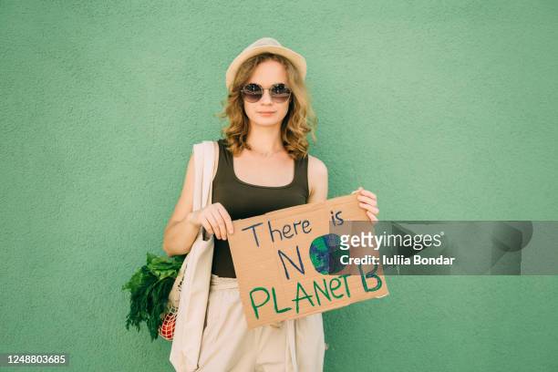 beautiful blonde girl holding there is no planet b over green background - letra b fotografías e imágenes de stock