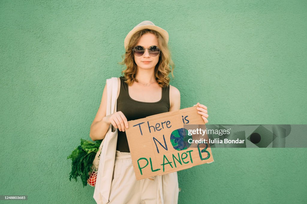 Beautiful blonde girl holding THERE IS NO PLANET B over green background