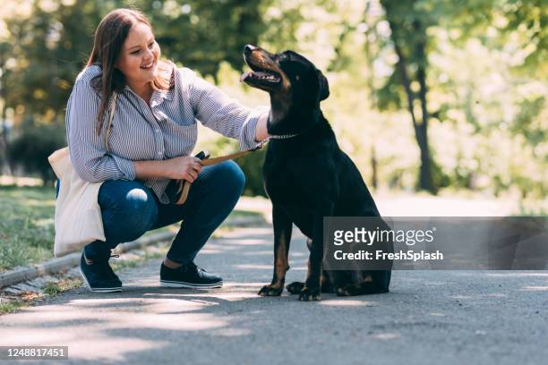 liefde en vriendschap: een gelukkige plus-grootte vrouw spelen met haar hond in een park - happy lady walking dog stockfoto's en -beelden