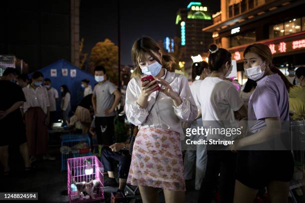 An animal vendor uses her iPhone at her stall at a night market on June 10, 2020 in Wuhan,Hubei Province,China.Wuhan has seen its urban life...
