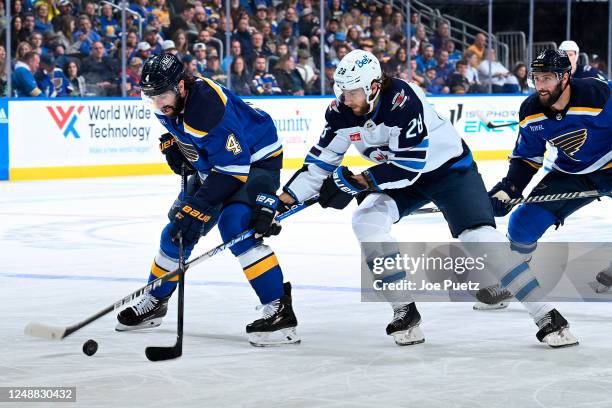 Nick Leddy of the St. Louis Blues and Kevin Stenlund of the Winnipeg Jets battle for the puck at the Enterprise Center on March 19, 2023 in St....