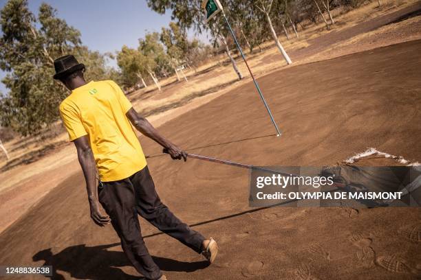 Golf employee passes the flag on the "brown", a mixture of sand and waste oil, at Ouagadougou's Golf Club, on February 21, 2023. - When Burkina Faso...