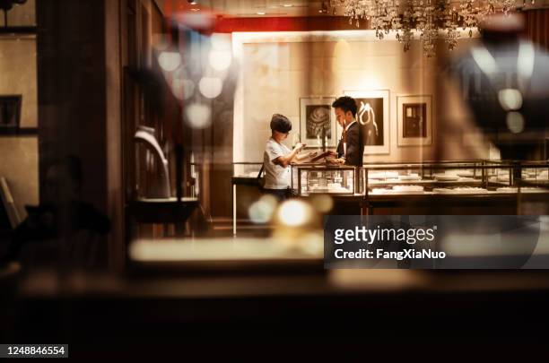 woman in luxury jewelry boutique viewing jewelry in front store manager - jeweller stock pictures, royalty-free photos & images