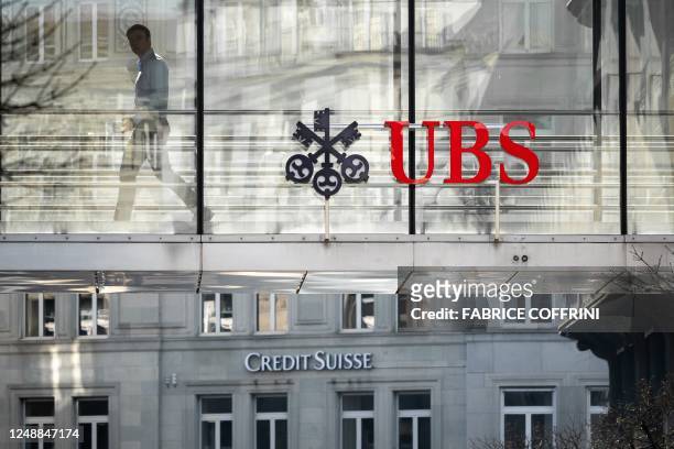 Employee is seen in silhouette with sign of Swiss giant banking UBS and a sign of Credit Suisse bank in Zurich on March 20, 2023. - Shares in...