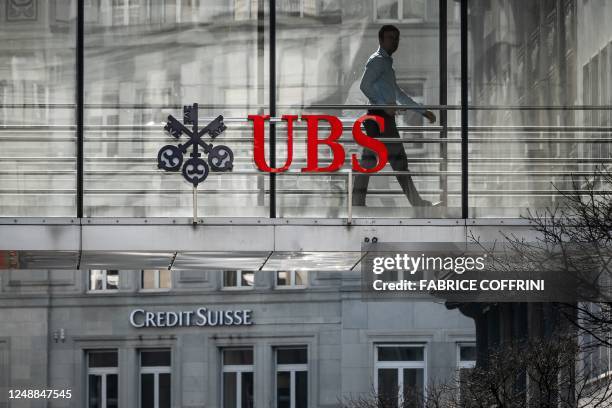 Employee is seen in silhouette with sign of Swiss giant banking UBS and a sign of Credit Suisse bank in Zurich on March 20, 2023. - Shares in...