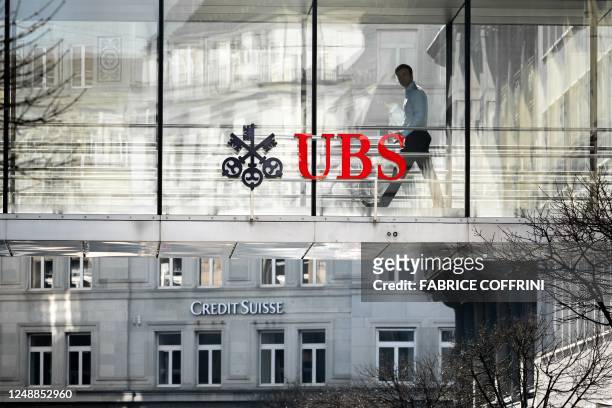Employee is seen in silhouette next to a sign of Swiss giant banking UBS and a sign of Credit Suisse bank in Zurich on March 20, 2023. - UBS share...