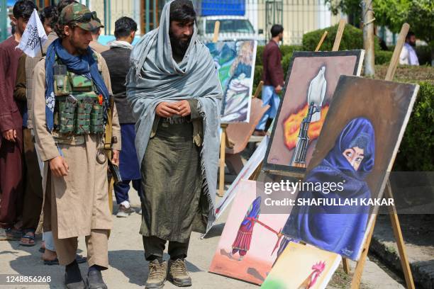 Taliban security personnel look at a portrait of a burqa-clad woman as they walk past a painting exhibition in Jalalabad on March 20, 2023.