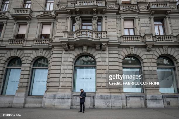 Man looks at his smartphone as he stands outside the headquarters of Credit Suisse bank in Zurich on March 20, 2023. - UBS agreed to take over Credit...