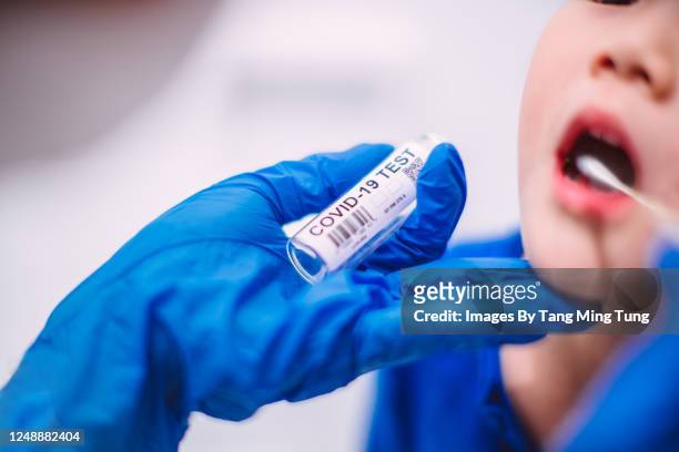 doctor’s hands in protection gloves putting covid-19 test swab into kid’s mouth - screening of child of grace arrivals stockfoto's en -beelden