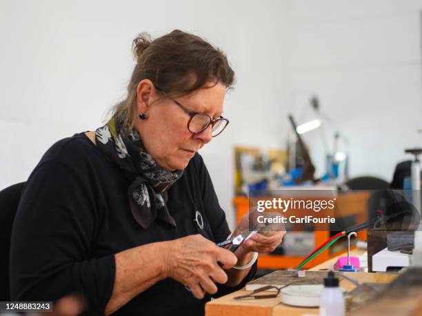 juwelier is in haar werkkamer met behulp van een soldeerbout om een zilveren ring te maken. - making jewelry stockfoto's en -beelden