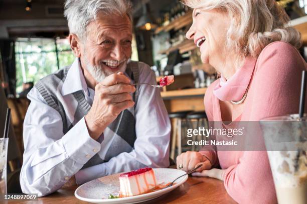 vrouw die echtgenoot met een plak van cake voedt - old couple restaurant stockfoto's en -beelden