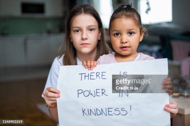 twee kleine meisjes die een affiche met handgeschreven bericht houden: er is macht in vriendelijkheid! - sociale rechtvaardigheid stockfoto's en -beelden