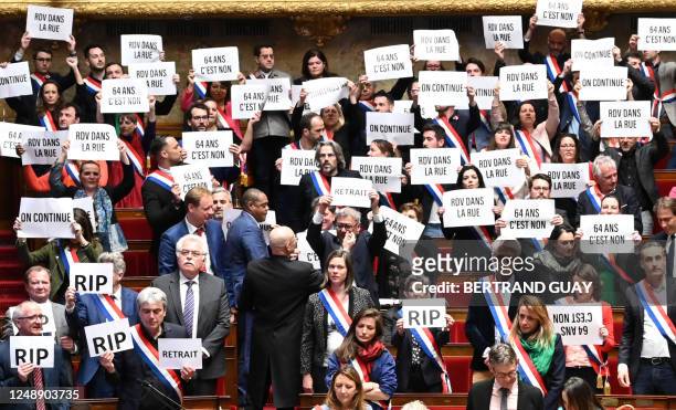 Members of National Assembly parliamentary group La France Insoumise and left-wing coalition NUPES hold signs reading "64 is a no", "See you in the...