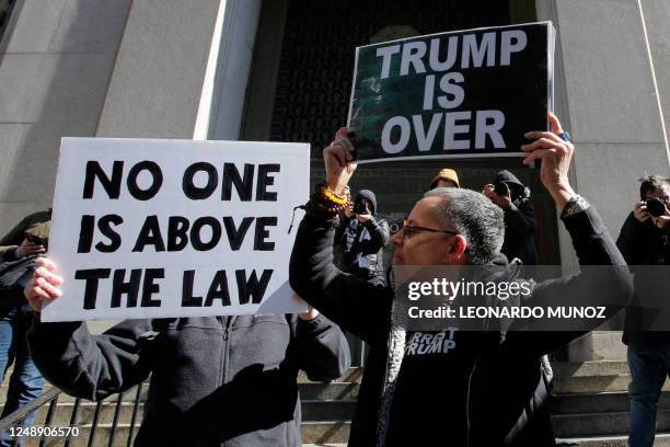 Anti-Trump demonstrators hold placards outside the Manhattan District Attorney's office in New York City on March 20, 2023. - Former US President...