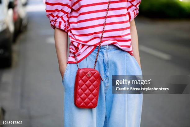 Red and pastel pink striped shirt by Steffen Schraut, light blue balloon denim jeans by Magda Butrym and a red cellphone bag by Chanel as a detail of...