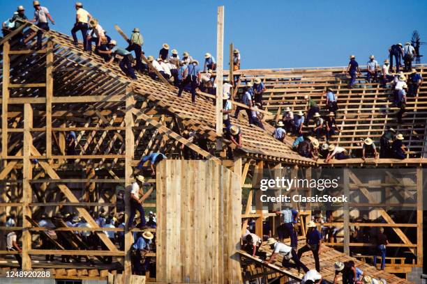 1980s Anonymous Group Of Amish Men Working Together Building Siding Roofing A Very Large Wood Timber Frame Barn Pennsylvania USA